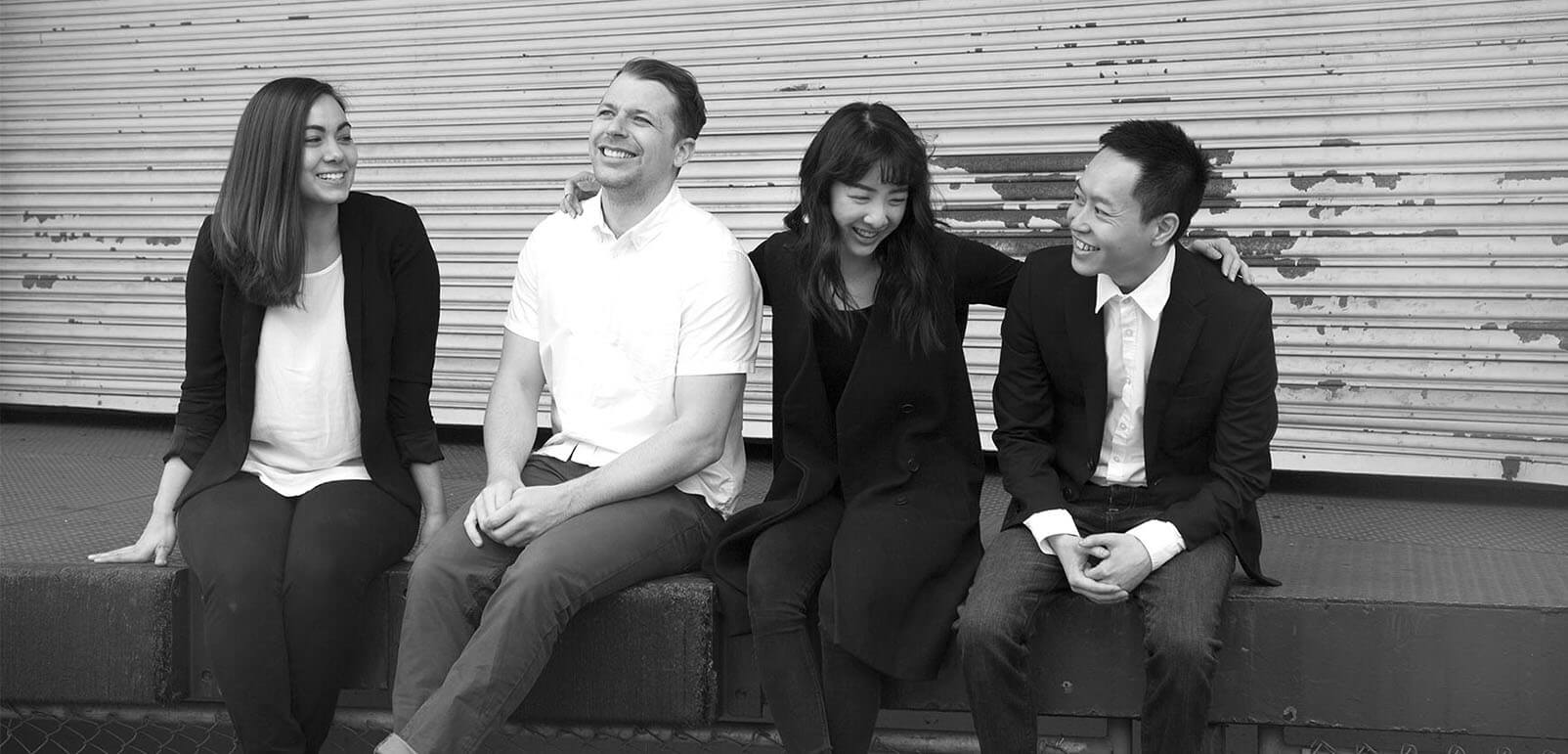 A black and white photo of Breanne, Joseph, Annette, and Bruce sitting together and chatting outside the studio